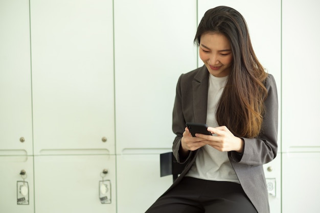 Jolie femme d'affaires en costume formel lisant un e-mail ou un SMS sur un téléphone mobile intelligent