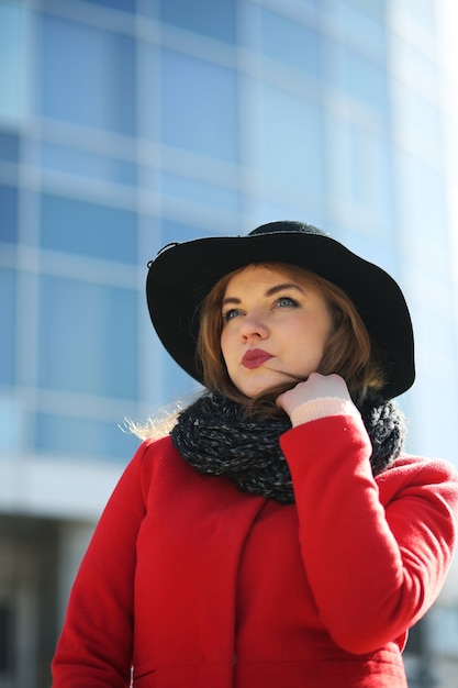 Jolie femme d'affaires dans un manteau rouge sur fond de gratte-ciel