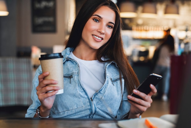 Jolie femme d'affaires est assise à table devant un ordinateur portable et parle sur téléphone mobile, négocie au téléphone.