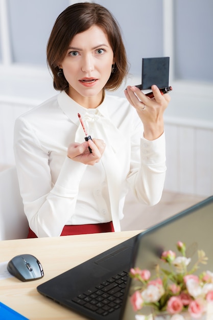 Jolie femme d'affaires faisant du maquillage au bureau