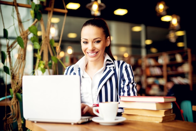 Jolie femme d'affaires moderne ayant une pause-café et à l'aide de son ordinateur portable.