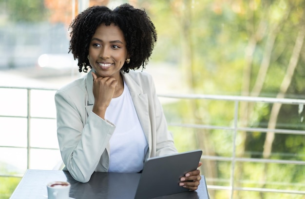 Jolie femme d'affaires noire assise au café à l'aide d'une tablette numérique