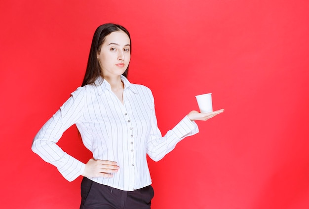 Jolie femme d'affaires posant avec une tasse de thé en plastique sur fond rouge.