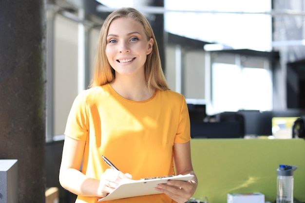 Jolie femme d'affaires regardant la caméra et souriante en se tenant debout au bureau.