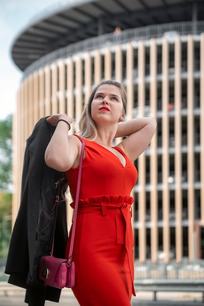 Jolie femme d'affaires en robe rouge et veste à la main sur fond d'autoroute et de centre d'affaires