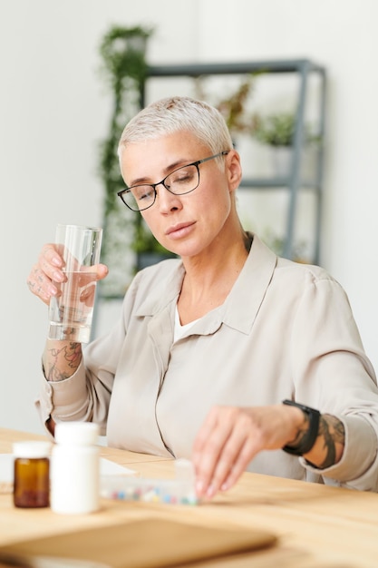 Jolie femme d'affaires tenant un verre d'eau tout en prenant des suppléments de biohacking au bureau nutrit