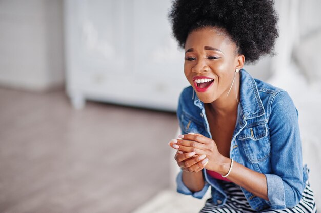 Jolie femme afro-américaine avec des cheveux afro portant une jupe et une veste en jean posée dans la salle blanche