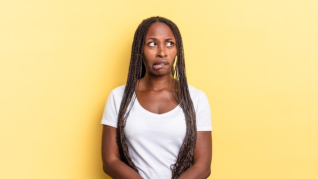 Jolie femme afro noire doutant ou pensant, se mordant la lèvre et se sentant peu sûre d'elle et nerveuse, cherchant à copier l'espace sur le côté