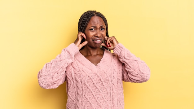 Jolie femme afro noire à la recherche de colère, de stress et d'agacement, couvrant les deux oreilles à un bruit assourdissant, un son ou une musique forte