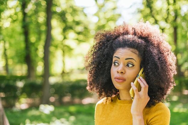 Jolie femme afro parlant au mobile, dans un jardin. Mise au point sélective.