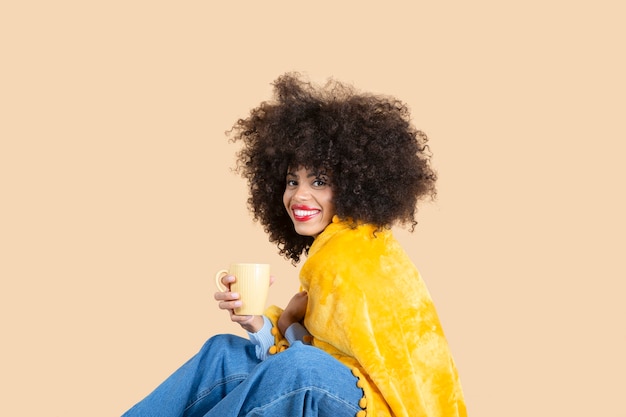 Jolie femme afro recouverte d'une couverture tout en prenant un café assis