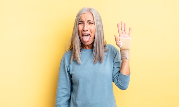 Jolie femme d'âge moyen avec une attitude joyeuse et rebelle, plaisantant et tirant la langue. concept de bandage à la main