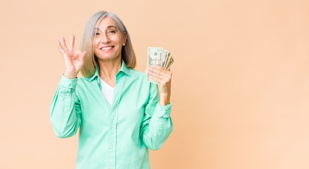 Jolie femme d'âge moyen avec des billets en dollars contre le mur de l'espace de copie