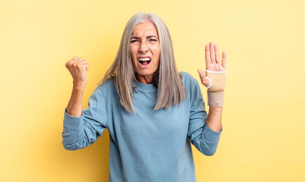 Jolie femme d'âge moyen criant agressivement avec une expression de colère. concept de bandage à la main