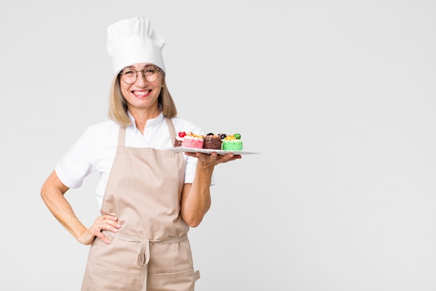 Jolie femme d'âge moyen avec des gâteaux contre le mur de l'espace de copie