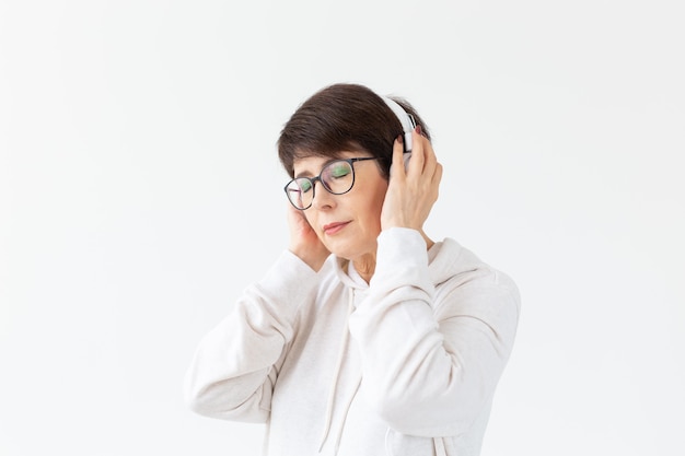Jolie femme d'âge moyen à lunettes et un pull blanc écoute sa musique préférée avec