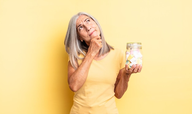 Jolie femme d'âge moyen pensant se sentir douteuse et confuse concept de bouteille de bonbons