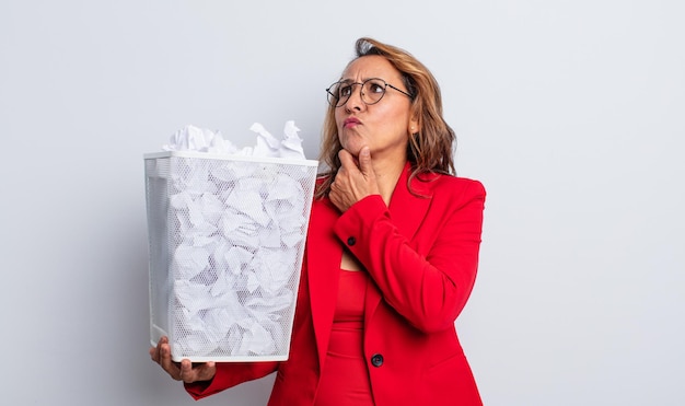 Jolie femme d'âge moyen pensant se sentir douteuse et confuse concept de poubelle de boules de papier