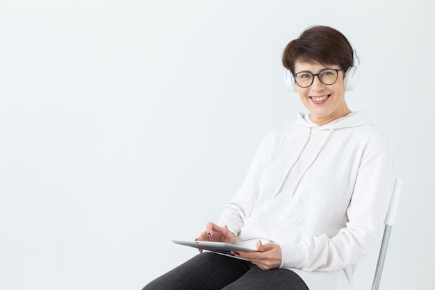 Jolie femme d'âge moyen positive en pull et lunettes écoute de la musique avec des écouteurs