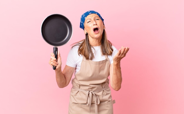 Jolie femme d'âge moyen à la recherche désespérée, frustrée et stressée et tenant une casserole. concept de chef