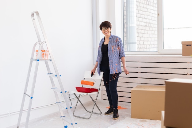 Jolie femme d'âge moyen avec rouleau à peindre à l'intérieur. Redécoration, rénovation, réparation d'appartement