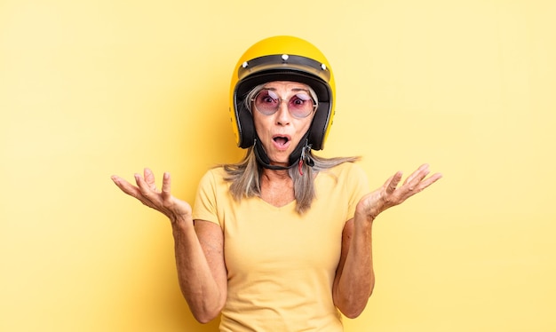 Photo jolie femme d'âge moyen se sentant extrêmement choquée et surprise. concept de casque de moto