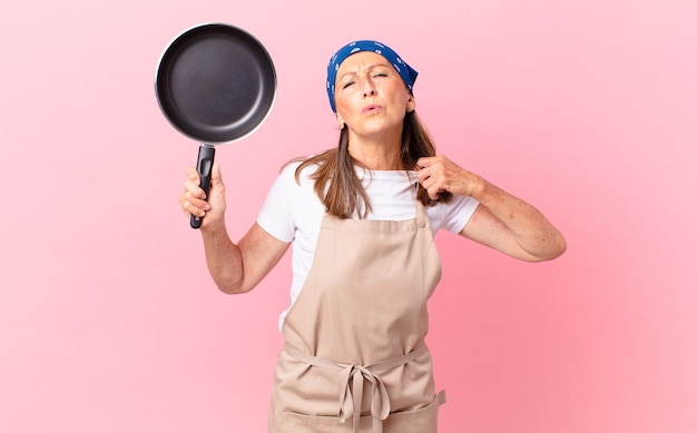 Jolie femme d'âge moyen se sentant stressée, anxieuse, fatiguée et frustrée et tenant une casserole. concept de chef