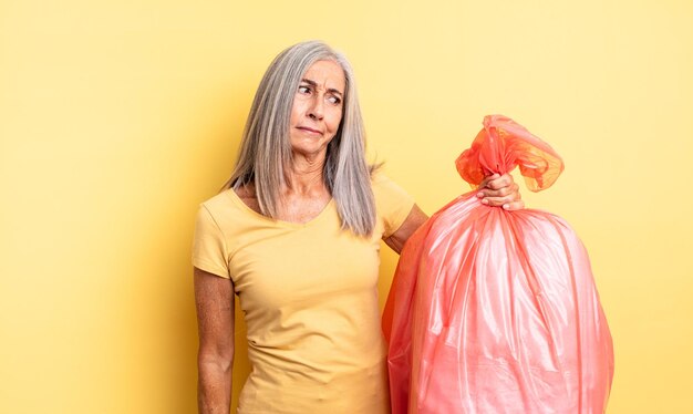 Jolie femme d'âge moyen se sentant triste bouleversée ou en colère et regardant sur le côté sac de garbaje en plastique