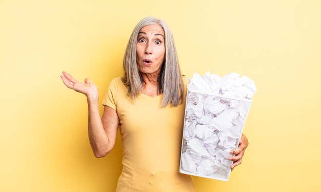 Jolie femme d'âge moyen semblant surprise et choquée, avec la mâchoire tombée tenant un objet. concept d'échec des boules de papier