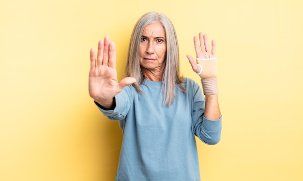 Jolie femme d'âge moyen à la sérieuse montrant la paume ouverte faisant un geste d'arrêt. concept de bandage à la main