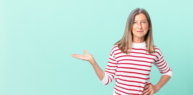 Jolie femme d'âge moyen souriant joyeusement avec une main sur la hanche et confiante