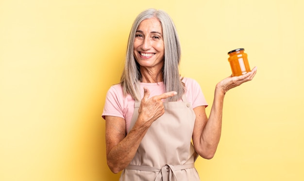 Jolie femme d'âge moyen souriant joyeusement, se sentant heureuse et pointant sur le côté. confiture de pêche