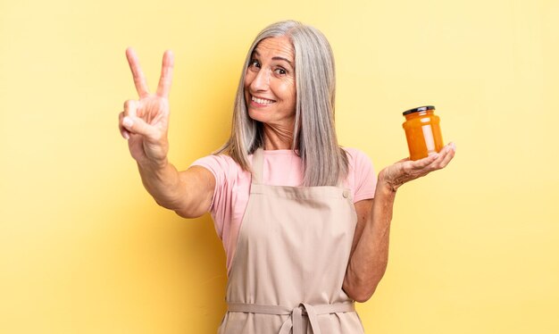 Jolie femme d'âge moyen souriante et semblant heureuse, gesticulant la victoire ou la paix. confiture de pêche