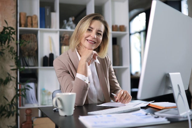 Jolie femme d'âge moyen travaillant au bureau, à l'aide d'un ordinateur de bureau contemporain.