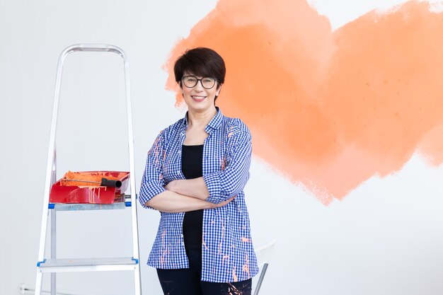 Jolie femme d'âge mûr souriante peinture mur intérieur de la maison avec rouleau à peinture. Redécoration