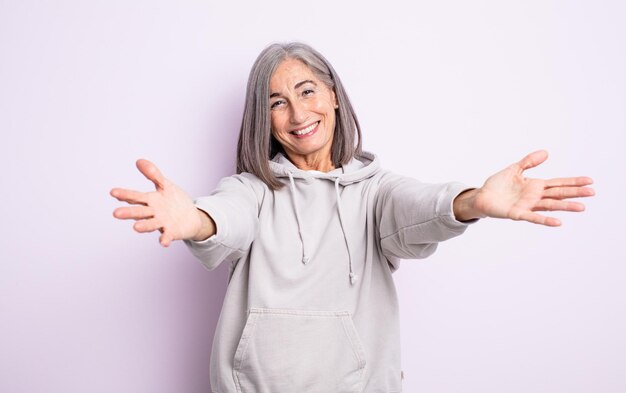 Jolie femme âgée souriant joyeusement donnant un câlin de bienvenue chaleureux, amical et affectueux, se sentant heureuse et adorable