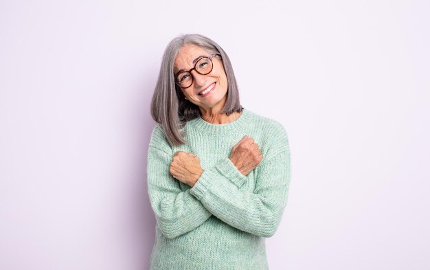 Jolie femme âgée souriante joyeusement et célébrant, les poings serrés et les bras croisés, se sentant heureuse et positive