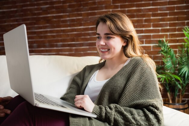 Jolie femme à l&#39;aide d&#39;un ordinateur portable allongé sur le canapé dans le salon