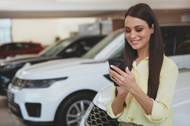 Jolie femme à l'aide de son téléphone intelligent tout en passant voiture neuve