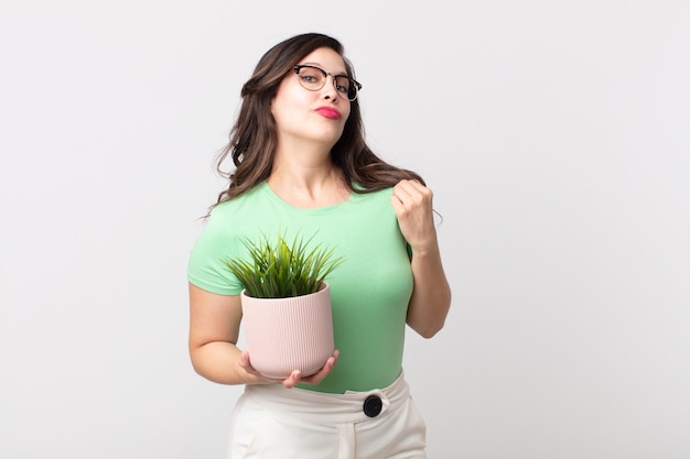 Jolie femme à l'air arrogante, réussie, positive et fière et tenant une plante décorative