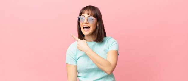 Jolie femme à l'air excitée et surprise pointant sur le côté et vers le haut pour copier l'espace