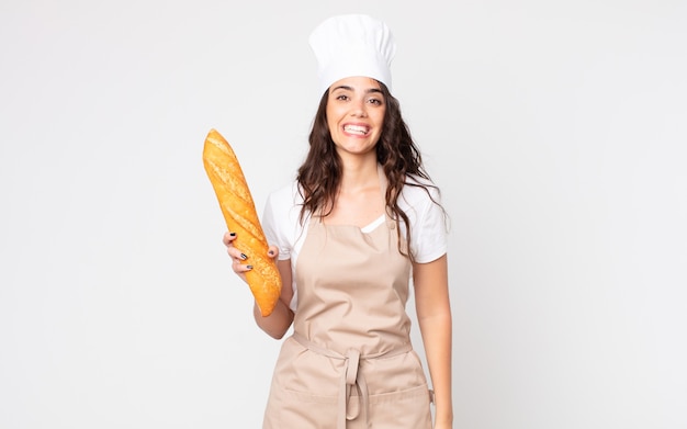 Jolie femme à l'air heureuse et agréablement surprise portant un tablier et tenant une baguette de pain