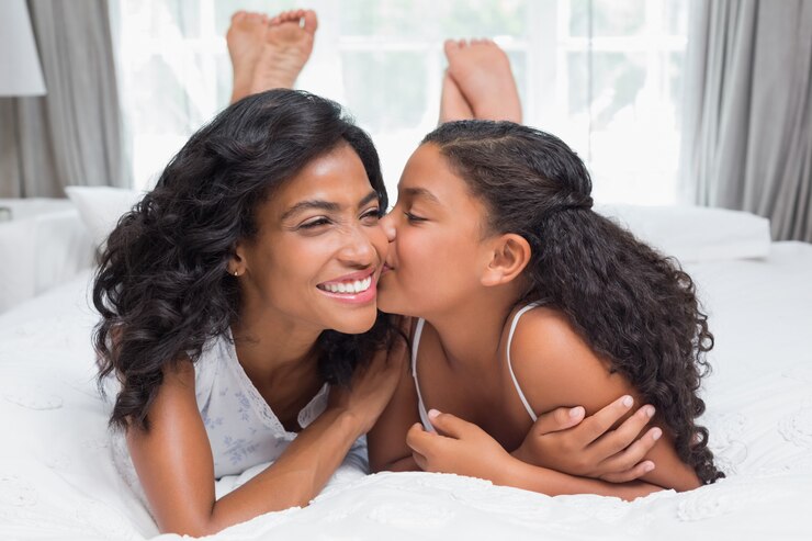 Photo jolie femme allongée sur le lit avec sa fille embrassant la joue