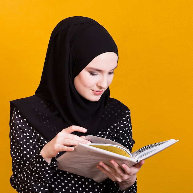 Photo jolie femme arabe, lecture de manuel sur fond jaune vif