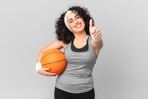 Jolie femme arabe se sentant fière, souriante positivement avec les pouces vers le haut et tenant un ballon de basket. notion de sport