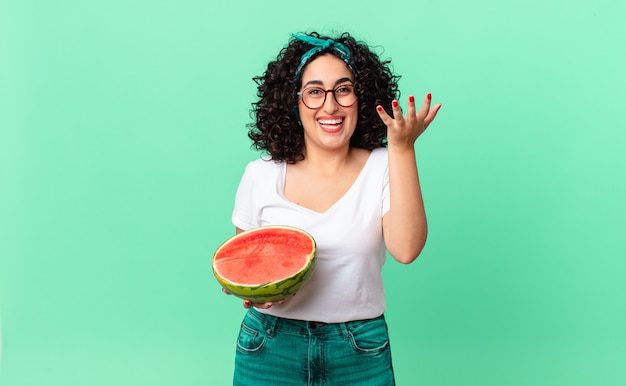 Jolie femme arabe se sentant heureuse, surprise de réaliser une solution ou une idée et tenant une pastèque. concept d'été