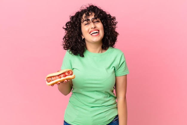 Jolie femme arabe semblant heureuse et agréablement surprise et tenant un hot-dog
