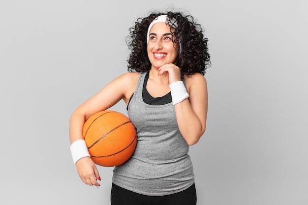 Jolie femme arabe souriant joyeusement et rêvant ou doutant et tenant un ballon de basket. notion de sport