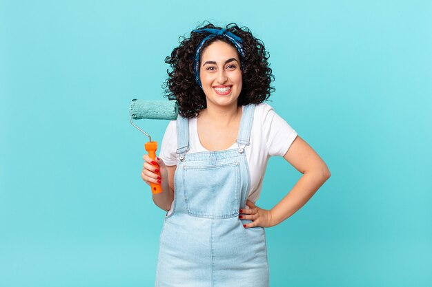 Jolie femme arabe souriante joyeusement avec une main sur la hanche et confiante. concept de maison de peinture