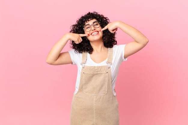 Jolie femme arabe souriante pointant avec confiance vers son propre large sourire